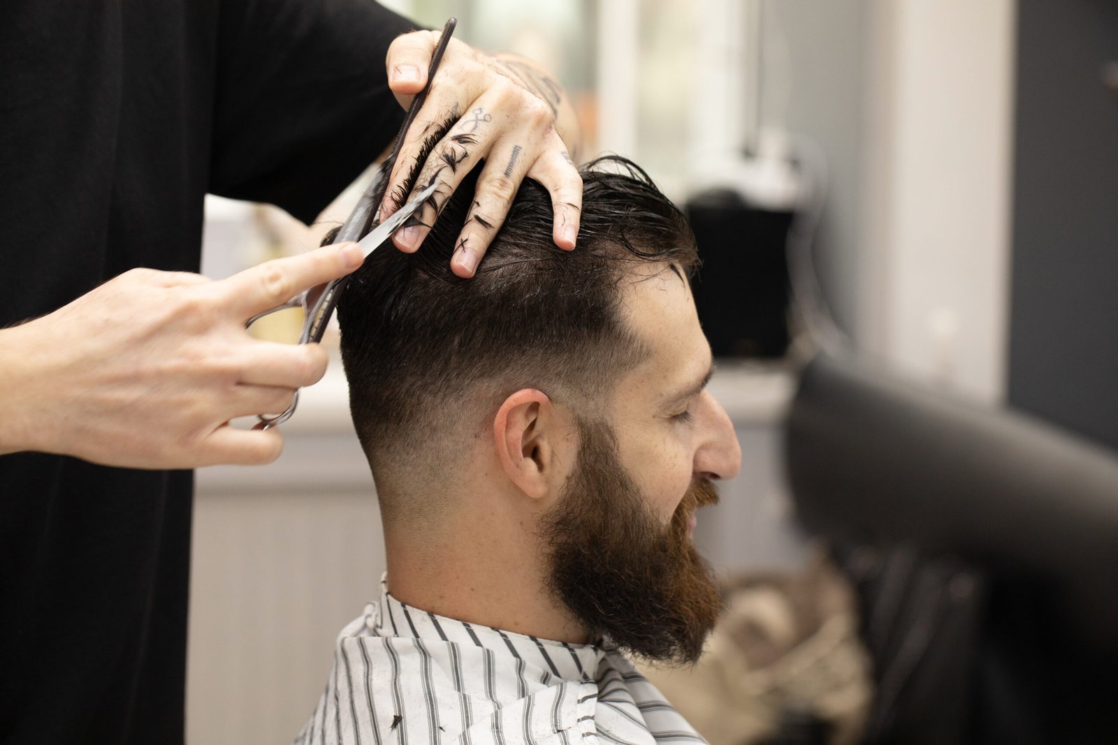 Handsome bearded man, having hair cut by scissors at barber shop